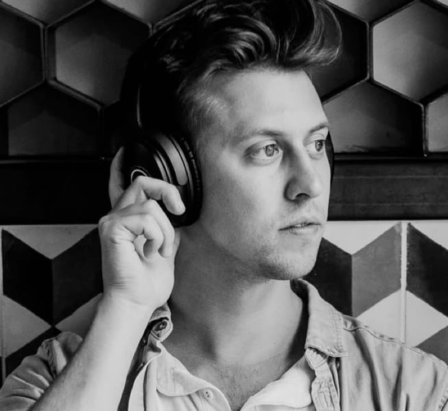 A man wearing a paid of headphones, holding his right hand up to to his ear.